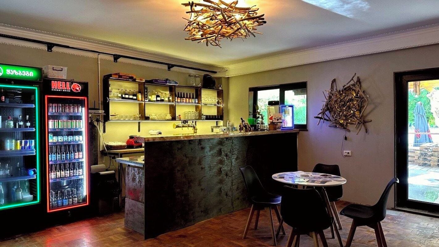 Una zona de bar con mostrador, taburetes y un refrigerador lleno de bebidas.