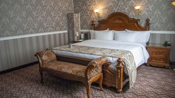 Una habitación de hotel con una cama grande, un banco de madera, una mesita de noche y una lámpara de pared.