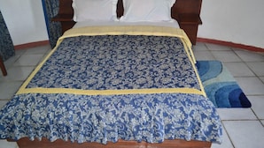 Un lit avec une couvre-lit à motifs et des oreillers, une tête de lit en bois et un tapis rayé bleu et jaune.