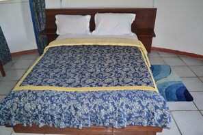 A bed with a patterned bedspread and pillows, a wooden headboard, and a blue and yellow striped rug. - Oceanic Beach Hotel (Kribi)