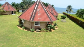 Un bungalow avec un toit rouge, entouré d’une pelouse bien entretenue et de palmiers, offrant une vue sur l’océan.
