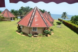 A bungalow with a red roof, surrounded by a well-maintained lawn and palm trees, with a view of the ocean. - Oceanic Beach Hotel (Kribi)