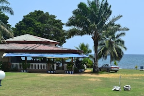 A beachfront property with a covered porch, a car parked nearby, and a palm tree. - Oceanic Beach Hotel (Kribi)