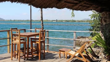 A wooden deck with a table and chairs, overlooking a body of water with a distant shoreline.
