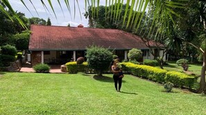 Uma casa com telhado de telhas vermelhas, rodeada por gramados verdes bem cuidados e diversos arbustos.