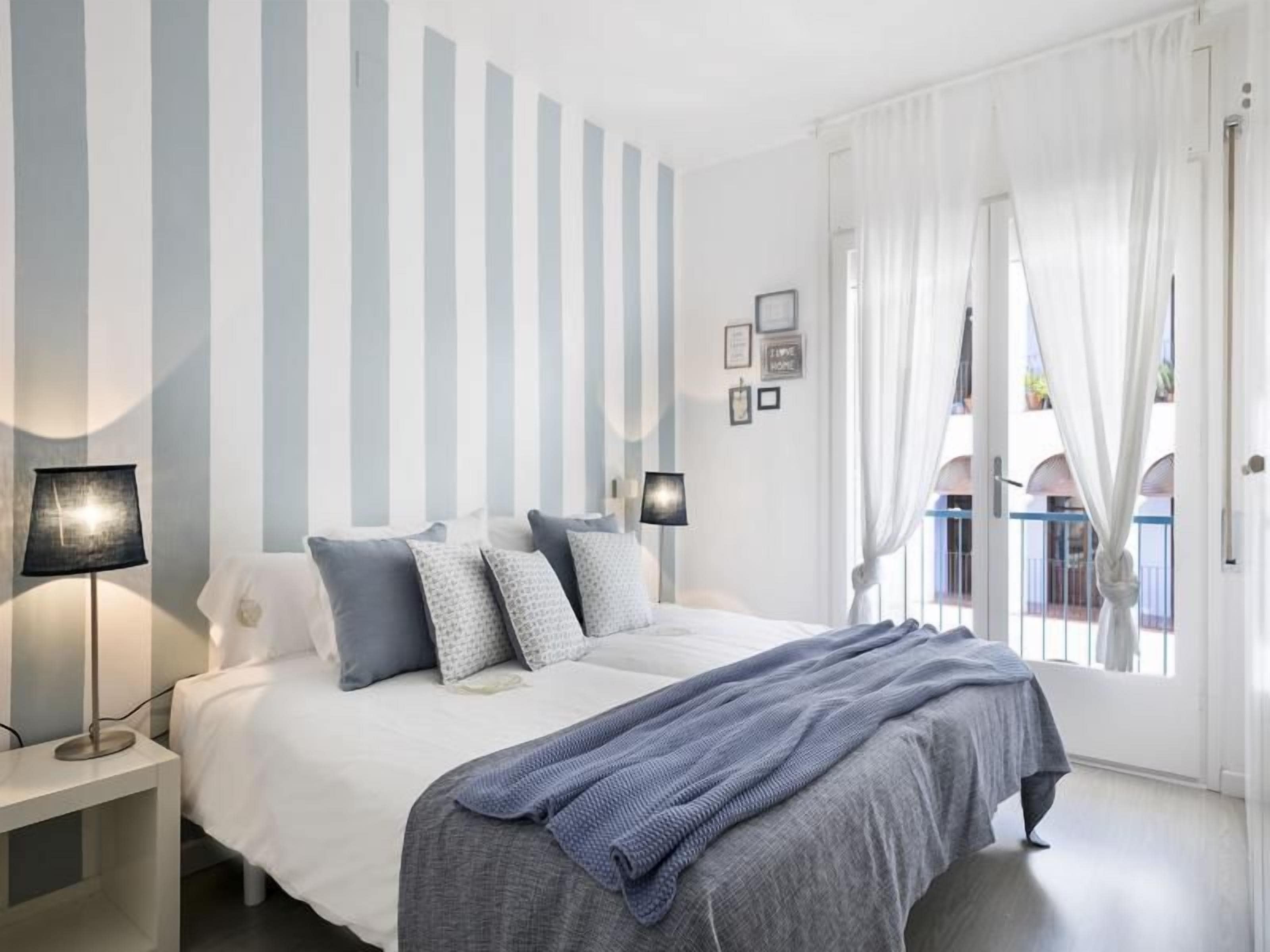 Un dormitorio con cama, lámparas de noche, una ventana con cortinas y vistas a un balcón exterior.