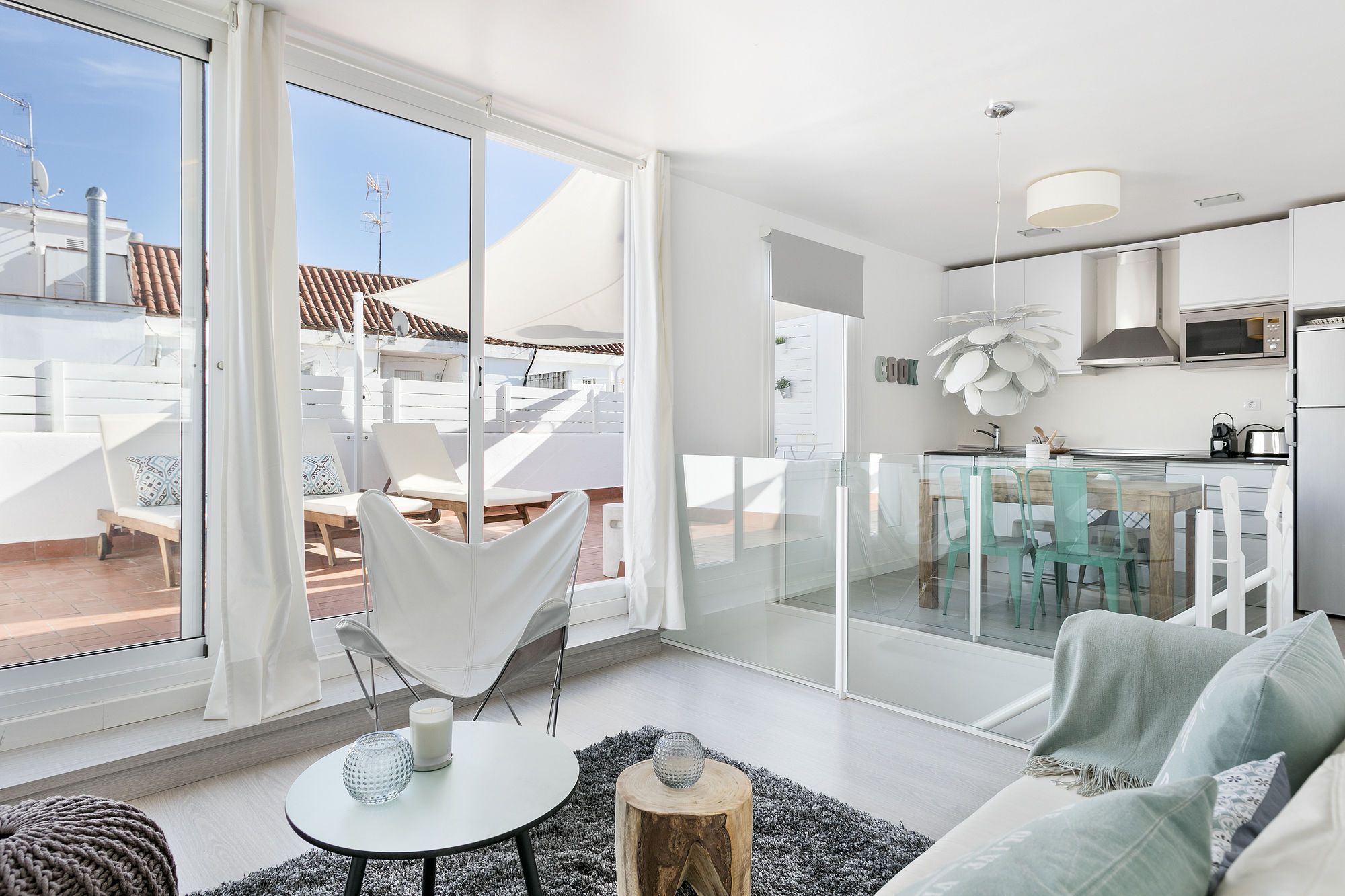 Un interior moderno con un comedor de vidrio, una sala de estar con sofá y mesa de centro, y una cocina con microondas y fregadero.