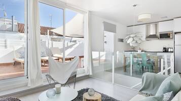 Un interior moderno con un comedor de vidrio, una sala de estar con sofá y mesa de centro, y una cocina con microondas y fregadero.