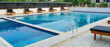 A rectangular swimming pool with a tiled deck, surrounded by lounge chairs and a covered seating area.