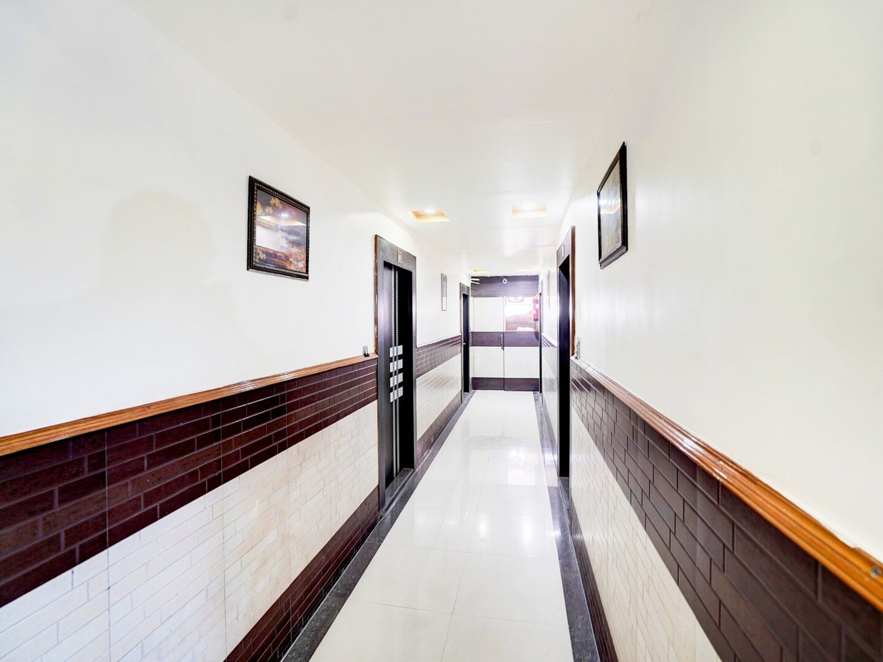 A hotel corridor with a tiled floor, wooden trim, and doors with a black handle.