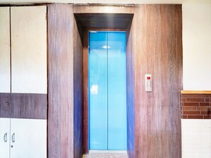 Un ascensor con interior azul, paredes de madera y un botón de emergencia rojo.