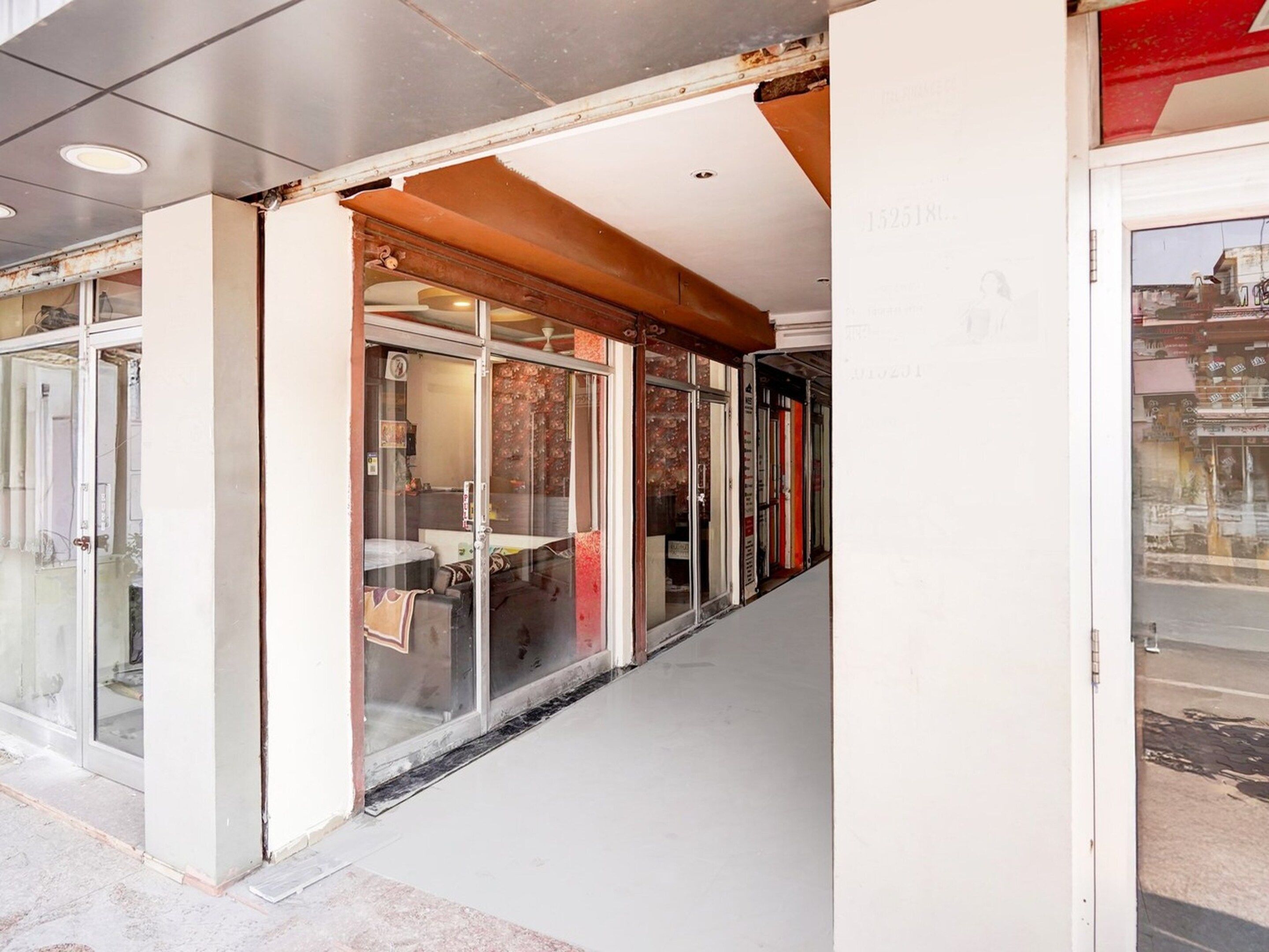 A corridor with glass doors leading to a room with a bed and a chair.