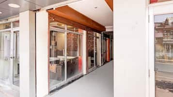 A corridor with glass doors leading to a room with a bed and a chair.