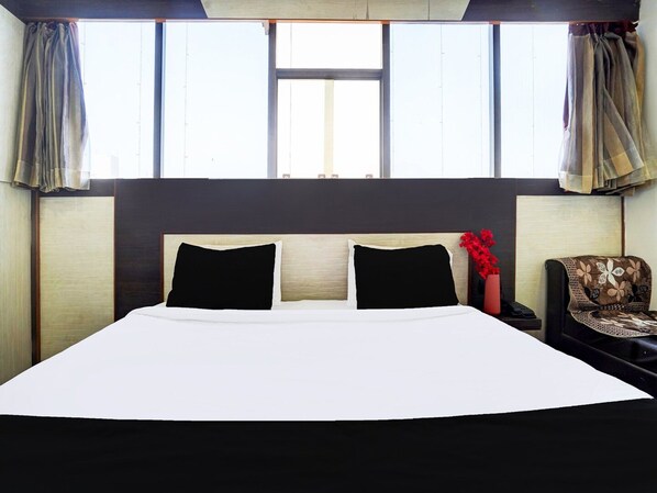 Habitación de hotel con una cama grande, dos almohadas negras, cabecera de madera, mesita de noche con teléfono y una silla con cojín estampado.