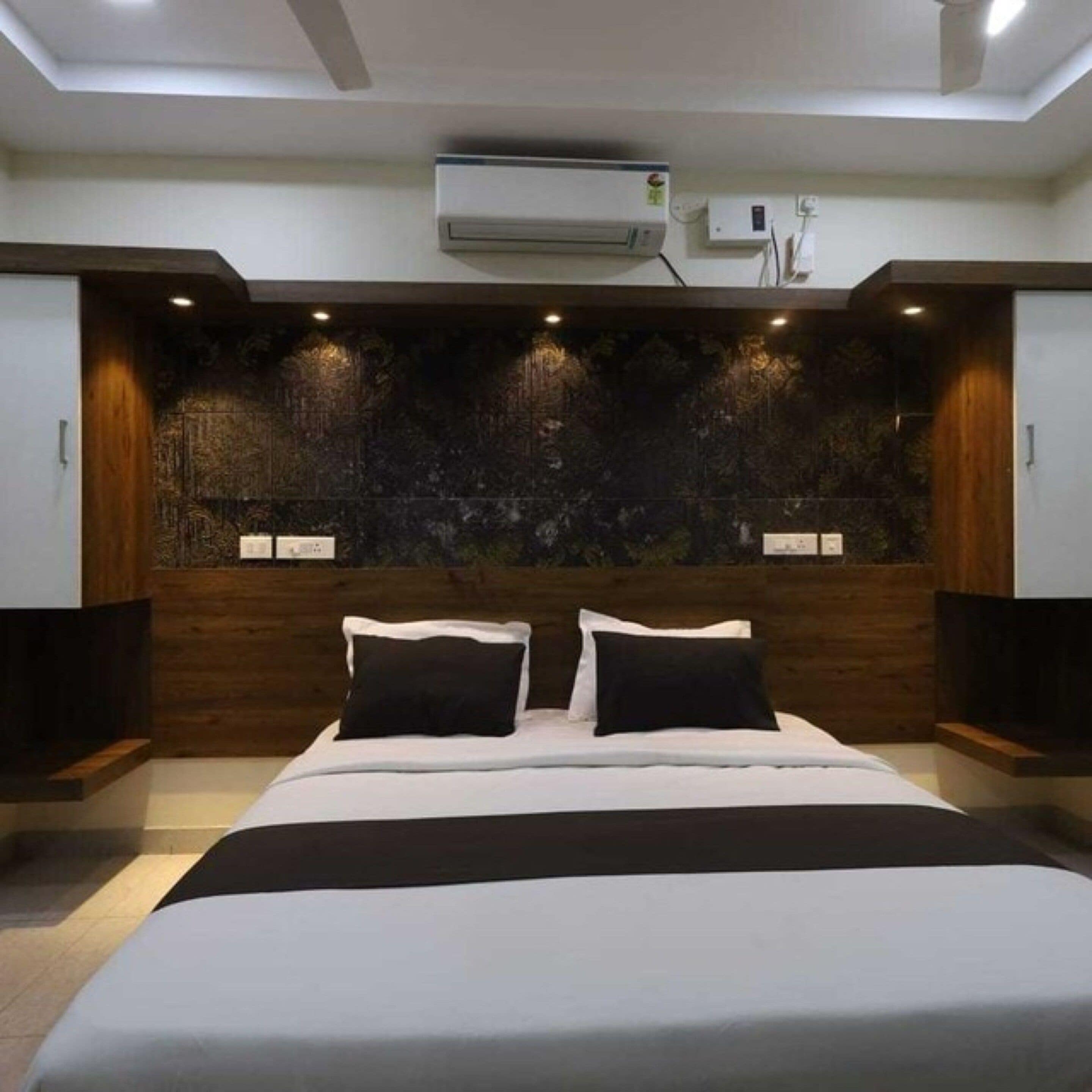 A modern bedroom with a large bed, dark wood paneling, and recessed lighting.
