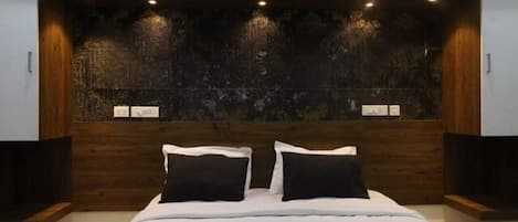A modern bedroom with a large bed, dark wood paneling, and recessed lighting.