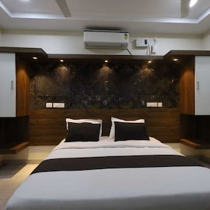 A modern bedroom with a large bed, dark wood paneling, and recessed lighting. - Deluxe Vishwa's Residency (Chennai)