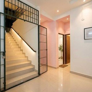 A staircase with a metal railing leading to a landing, a door with a mat, and a framed picture on the wall. - Deluxe Vishwa's Residency (Chennai)