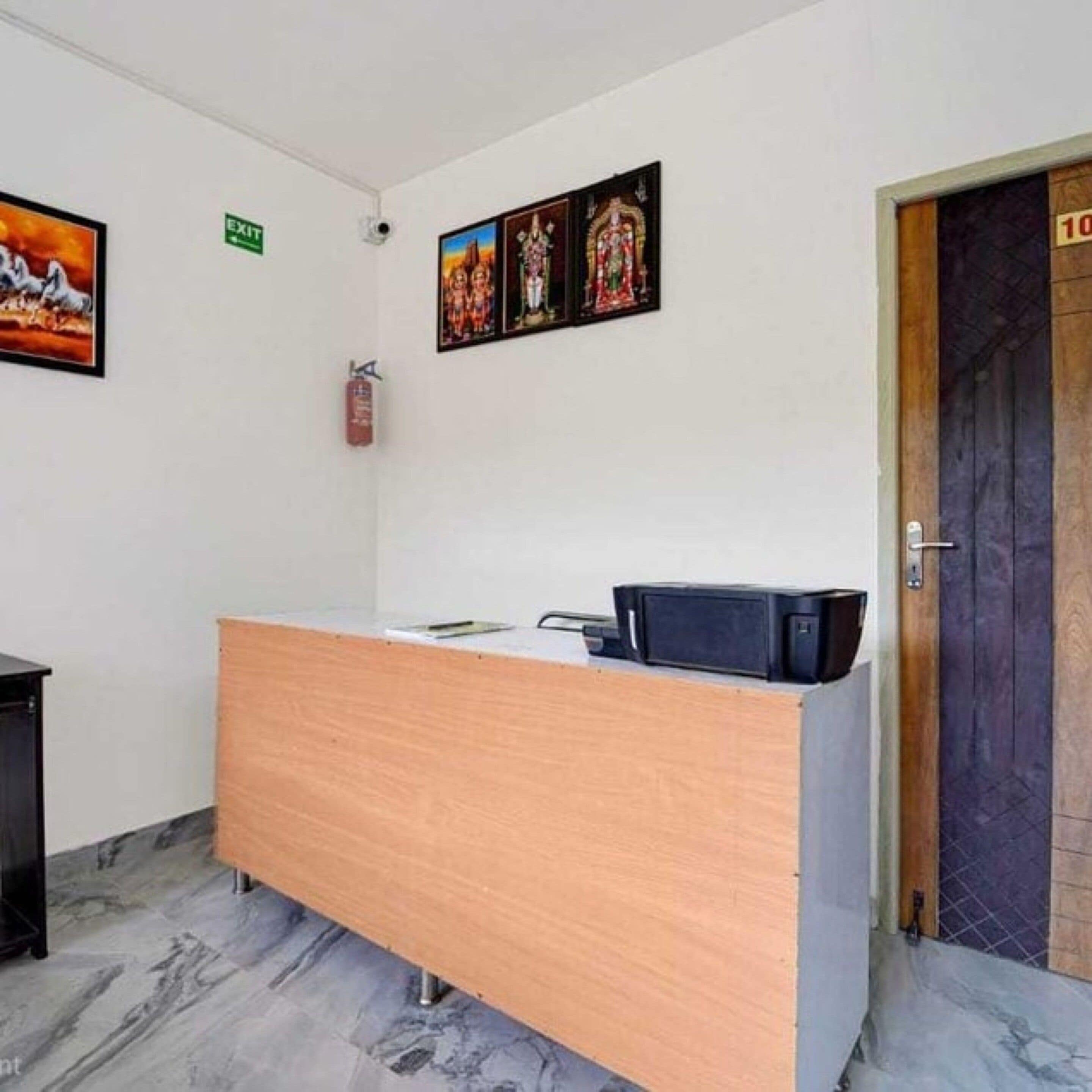Un mostrador de recepción con detalles de madera, un extintor de incendios montado en la pared y una puerta con placa de número.