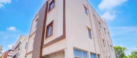 Un edificio residencial moderno de varios pisos con techo plano, ventanas amplias y un acceso de garaje visible.