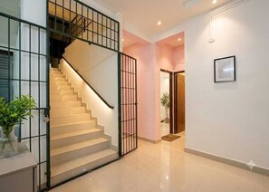 A staircase with a metal railing leading to an upper floor, a hallway with a door, and a potted plant. - Deluxe Vishwa's Residency (Chennai)