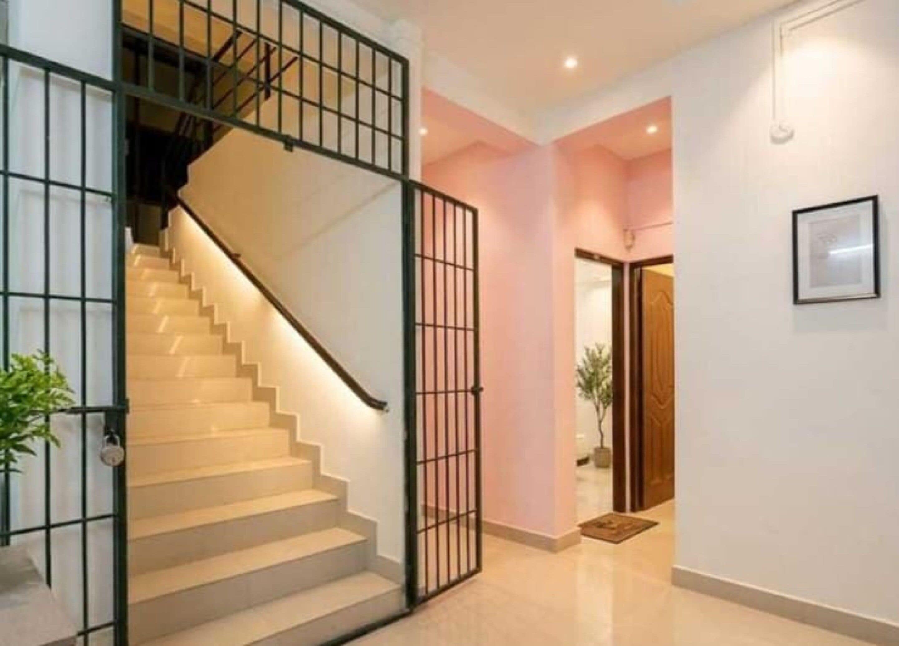 Una escalera con barandilla de metal que lleva a un rellano, una puerta con un panel decorativo y un cuadro en la pared.