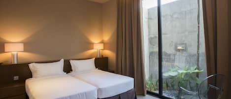 A hotel room with a double bed, two bedside lamps, a large window with curtains, a small table, and a chair.