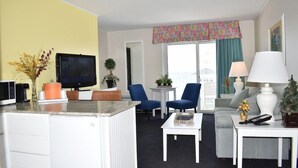 A hotel room with a kitchenette, a flat-screen TV, a sofa, two chairs, a small table, and a window with curtains. - The Breakers Resort Lakeside (St Ignace)