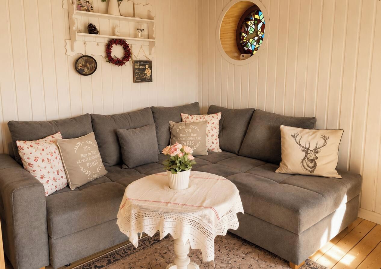 Ein gemütliches Wohnzimmer mit einem grauen Sofa, einem runden Tisch mit einer weißen Spitzenleinentischdecke und dekorativen Kissen.