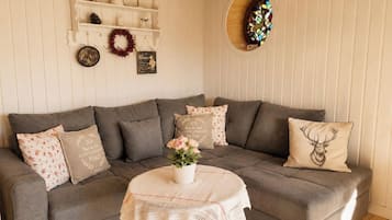 Uma sala de estar aconchegante com um sofá cinza, uma mesa redonda com toalha de renda e almofadas decorativas.