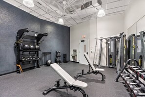 Une salle de sport équipée de matériel de musculation, de bancs et d’un support mural pour les kettlebells et les haltères.