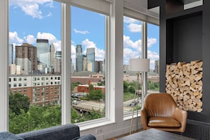 A room with large windows, a leather chair, a lamp, and a stack of firewood. - 1Bd Condo in Downtown Minneapolis | Minutes from Convention Center and Stadium (Minneapolis)
