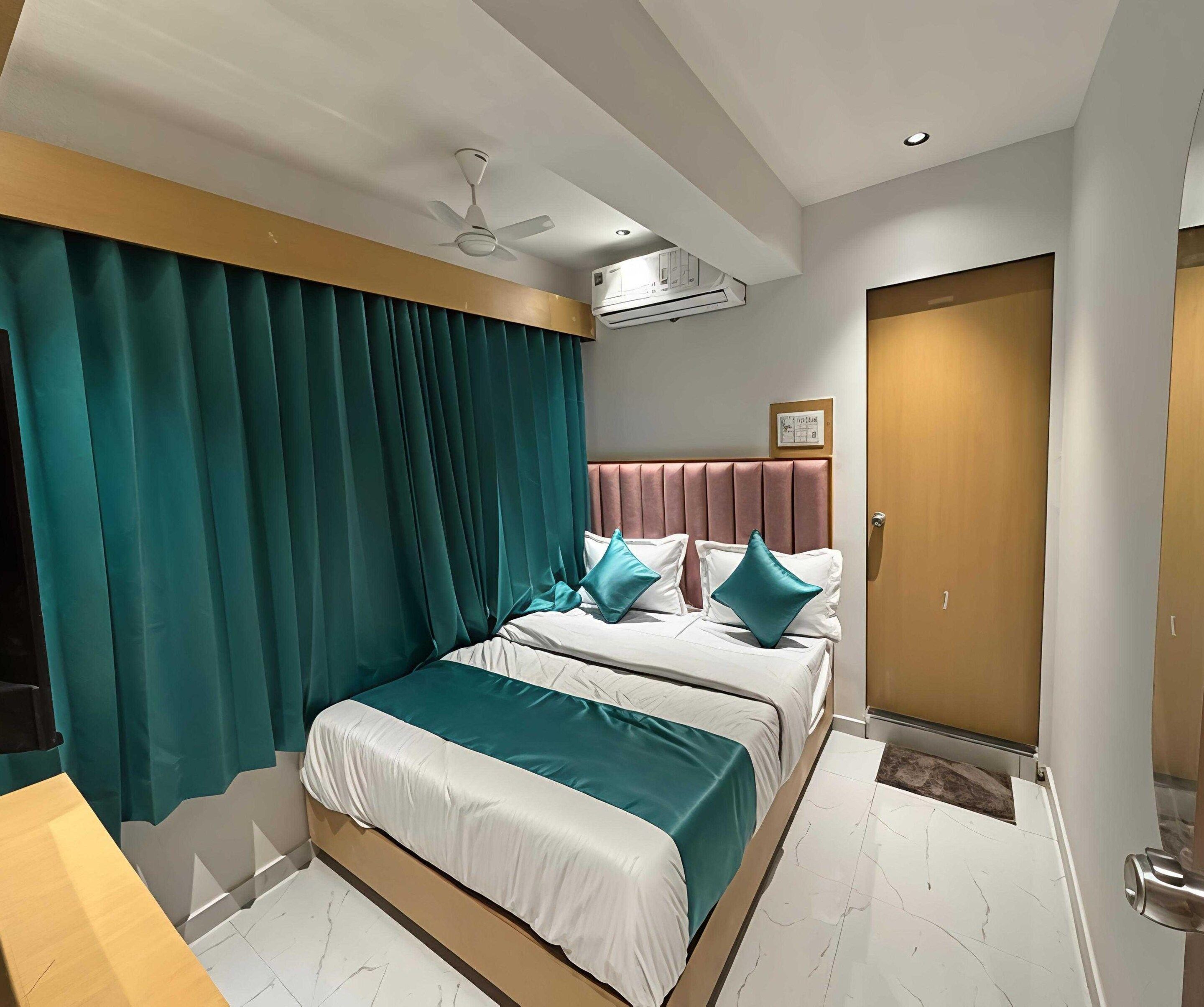 A hotel room with a bed, two pillows, a ceiling fan, an air conditioning unit, and a door.