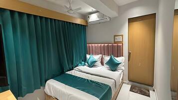 A hotel room with a bed, two pillows, a ceiling fan, an air conditioning unit, and a door.