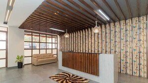 Un área de recepción con techo de listones de madera, un sofá, una cortina estampada y una alfombra en el suelo.