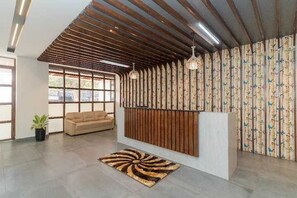 A reception area with a wooden slatted ceiling, a sofa, a patterned curtain, and a floor rug. - Deluxe With Balcony Hotel Prime Bliss (Bengaluru)
