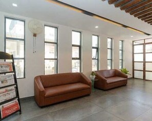 A modern interior with two leather sofas, large windows, and a wall-mounted fan. - Deluxe With Balcony Hotel Prime Bliss (Bengaluru)