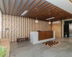 A reception area with a wooden reception desk, patterned curtains, a patterned rug, and a hanging light fixture. - Deluxe With Balcony Hotel Prime Bliss (Bengaluru)