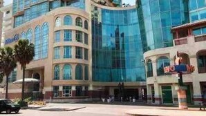 A high-rise hotel with a modern glass facade, multiple balconies, and a prominent corner entrance. - Apartamento de Lujo Frente al Mar con Jacuzzi (Santo Domingo)