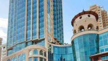 A high-rise hotel with a modern glass facade, multiple balconies, and a prominent corner entrance.