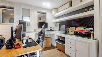 A modern kitchen with a dining area, equipped with a computer, gaming console, and various kitchen appliances.