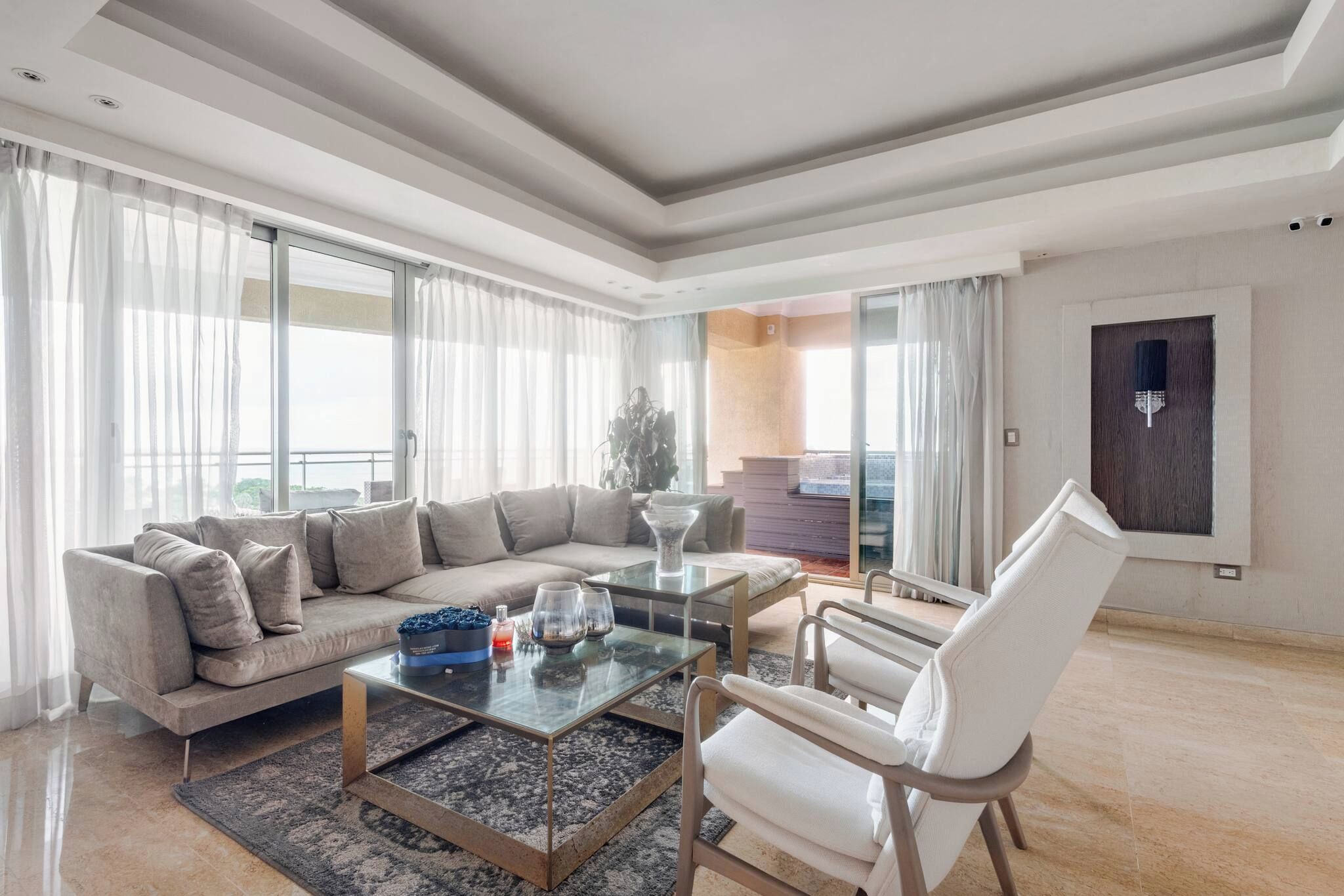 A modern living room with a sectional sofa, a glass coffee table, and a white armchair.