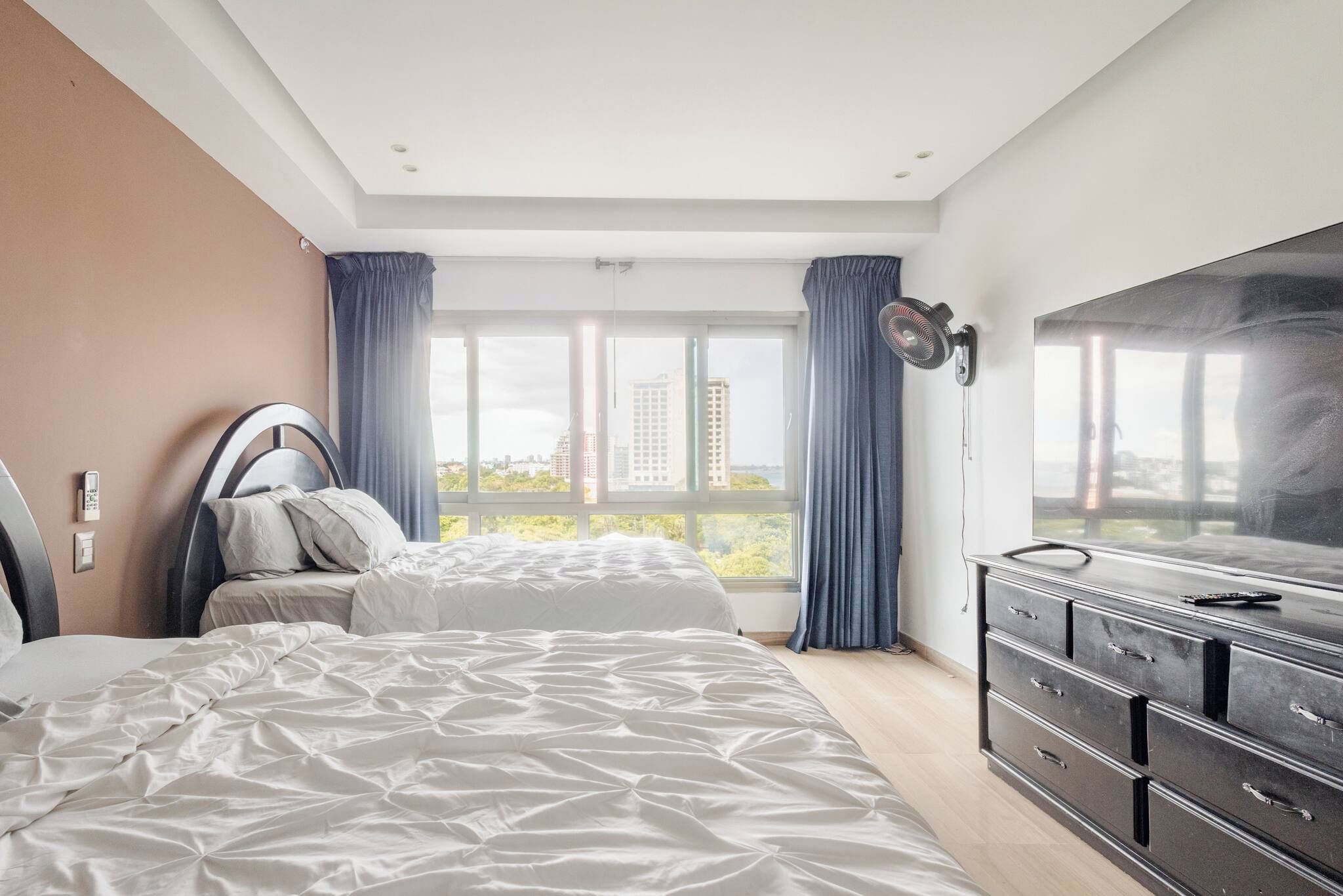 A bedroom with a bed, a dresser, a TV, and a window with curtains.
