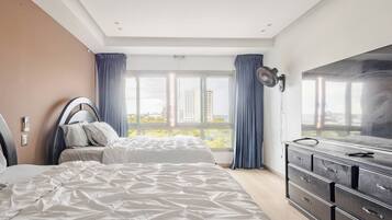 A bedroom with a bed, a dresser, a TV, and a window with curtains.