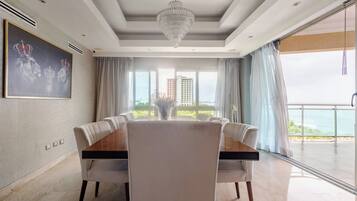 A modern dining room with a large table and chairs, a chandelier, and a view of the sea.