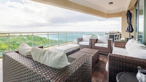 A balcony with wicker furniture, a grill, and a view of the ocean. - Apartamento de Lujo Frente al Mar con Jacuzzi (Santo Domingo)