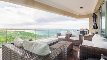 A balcony with wicker furniture, a grill, and a view of the ocean.