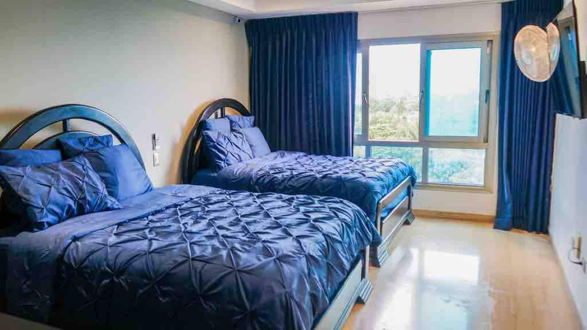 A bedroom with two beds, a large window, and blue curtains.