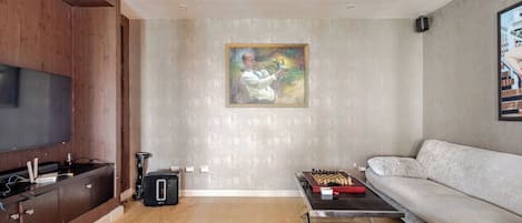 A modern living room with a flat-screen TV, a coffee table with a chess set, a sofa, and a painting on the wall.