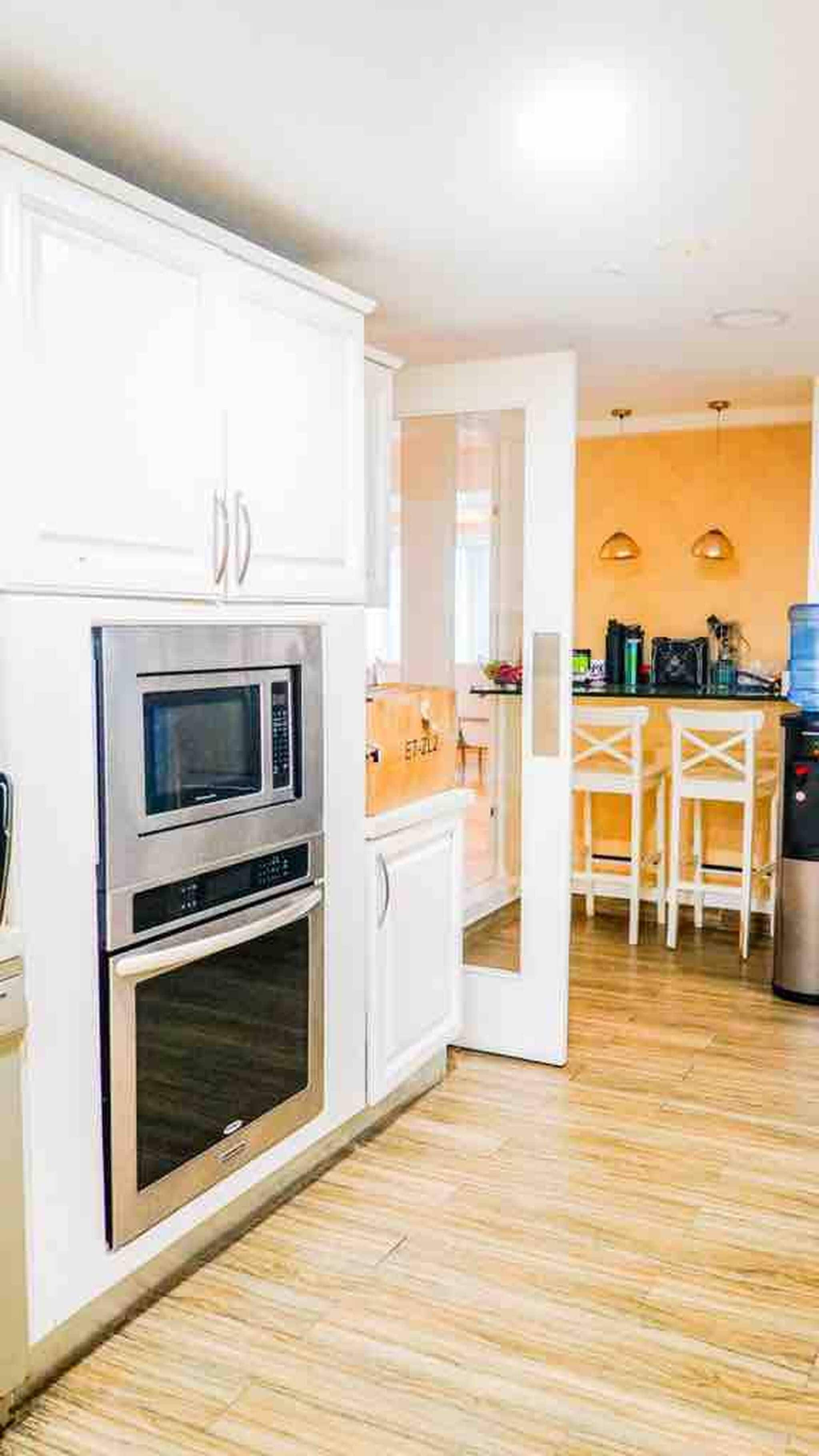 A kitchen with white cabinets, a microwave, and an oven. There is a dining area with a table and chairs.